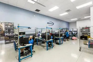 AGS Devices employess working at their workstations, with a large AGS Devices logo prominently displayed on the wall.